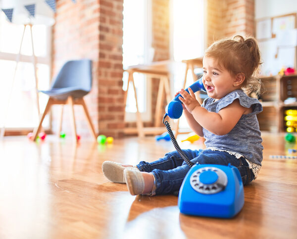 Beautiful toddler sitting on the floor playing with vintage phone at kindergarten